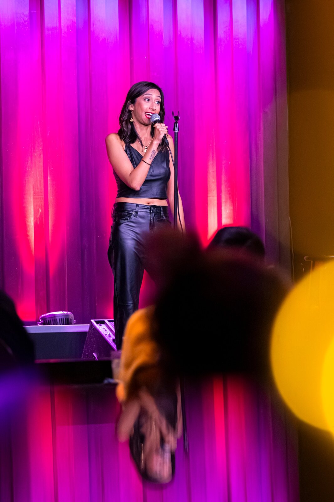 Priya performing comedy on stage with a microphone